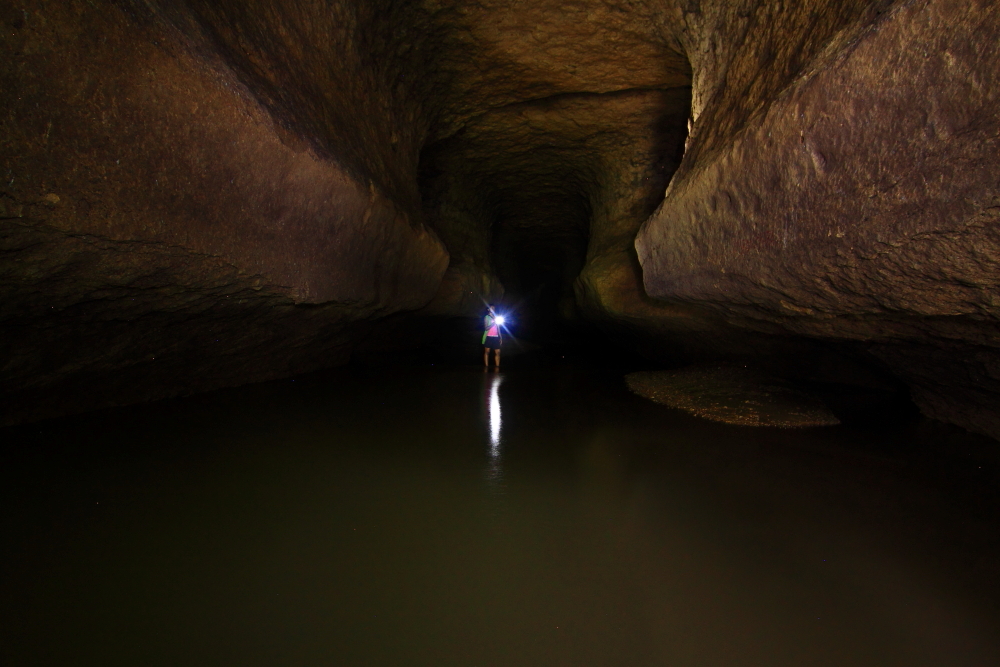 Picture of caving where a river is flowing inside the cave.